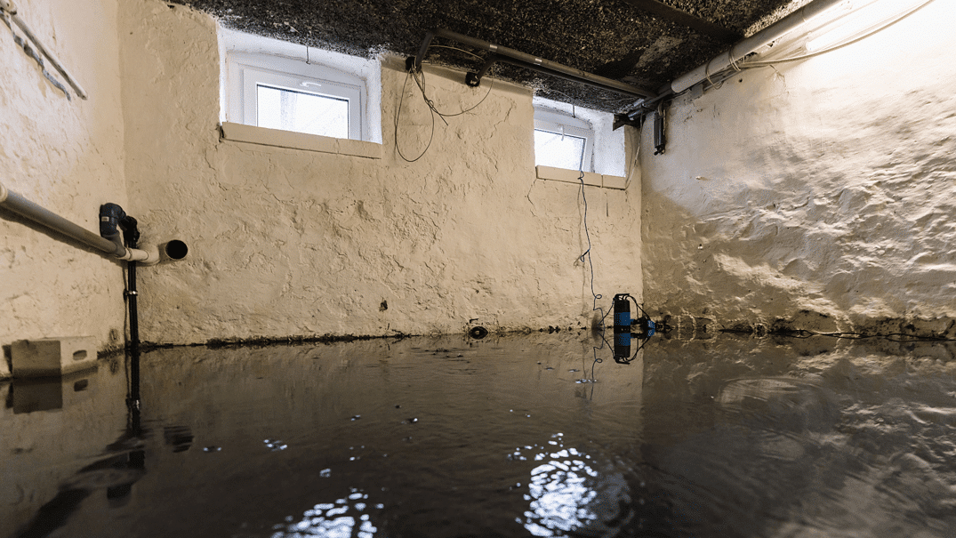 Basement flood with standing water, exposed pipes and a sump pump indicating water damage
