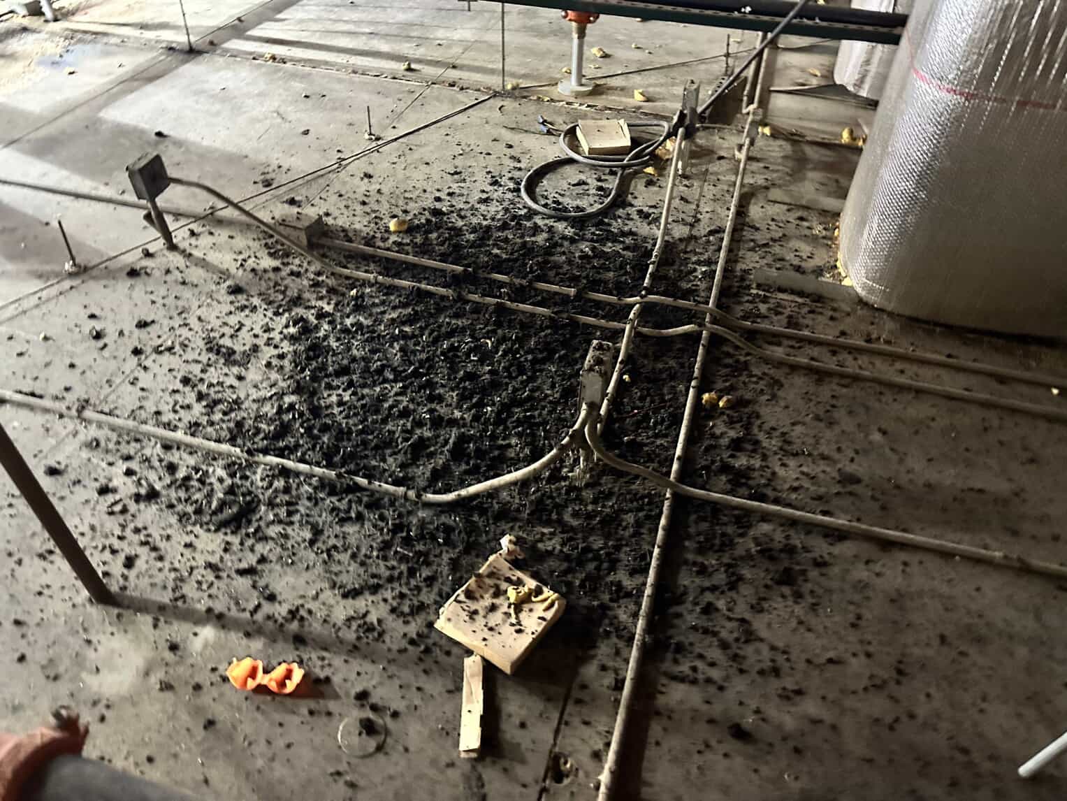 Black insulation debris scattered around exposed electrical conduits and cables on concrete construction floor