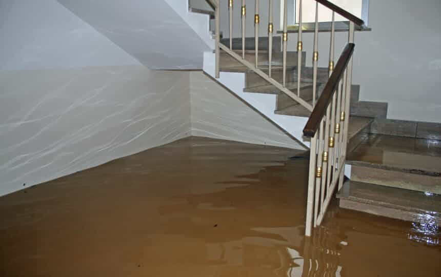 Basement stairwell partially submerged in muddy brown floodwater, wet tiled steps and metal railing.