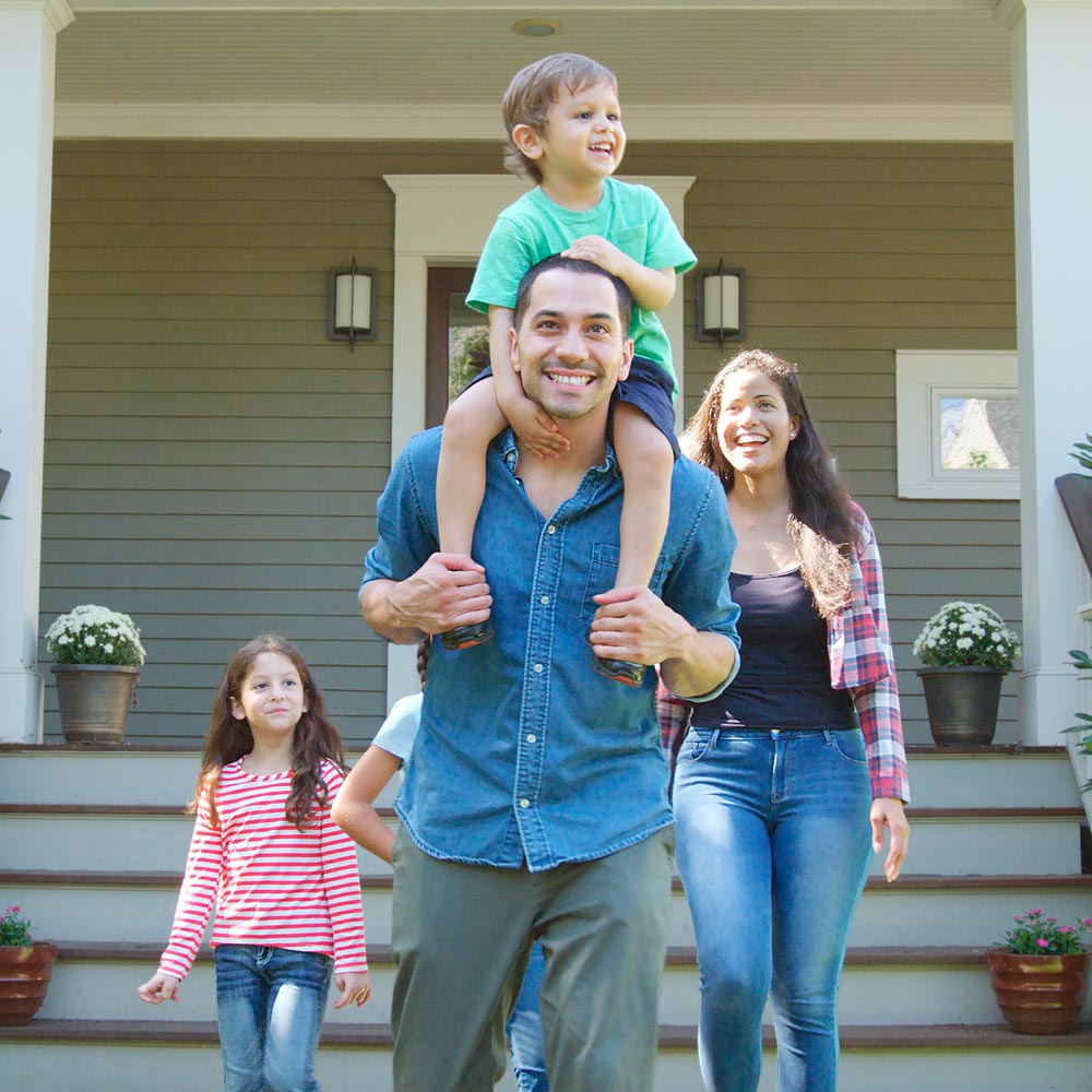 Smiling family walking down front steps, father carries young boy on shoulders with mother and daughter following