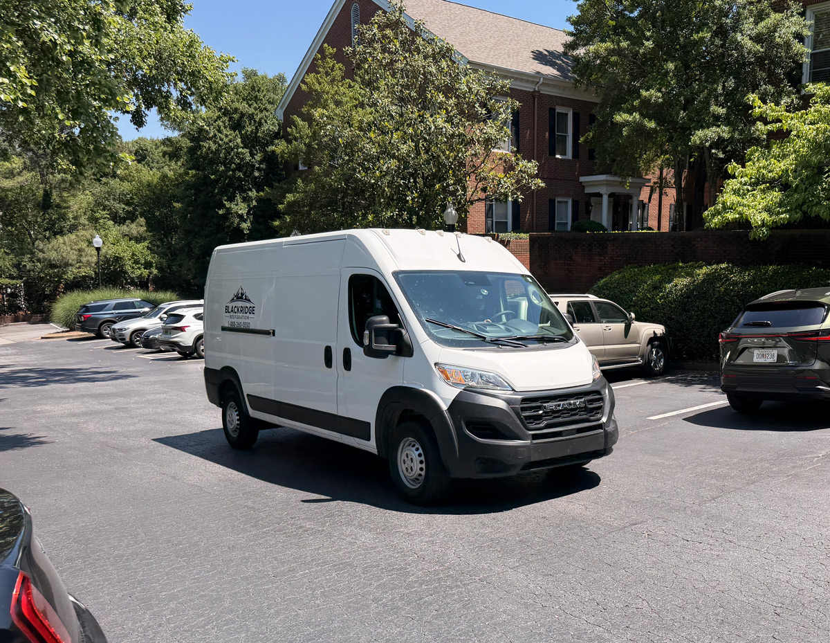 White Blackridge cargo van parked in a sunlit apartment parking lot beside brick building and trees