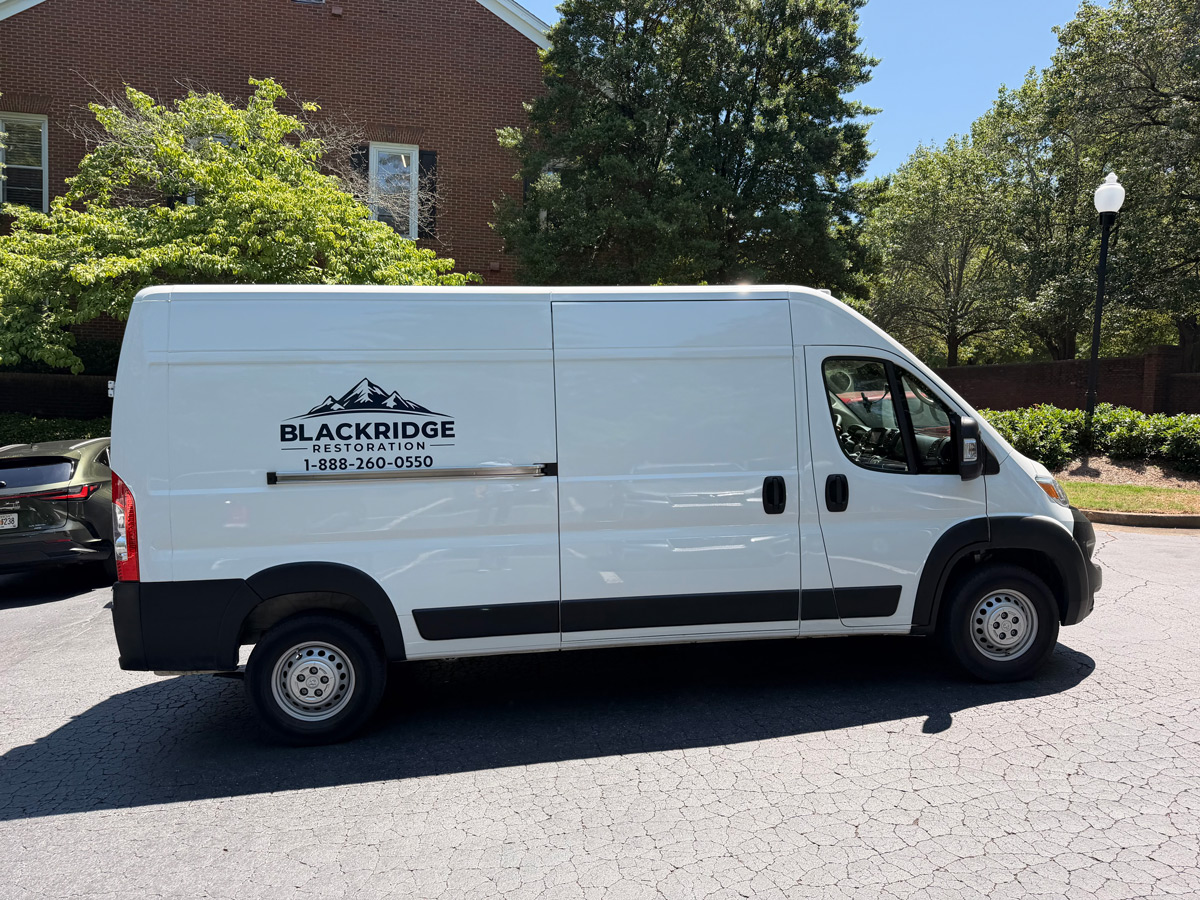 White cargo van with Blackridge Restoration logo and phone number 1-888-260-0550 parked by a brick building and trees