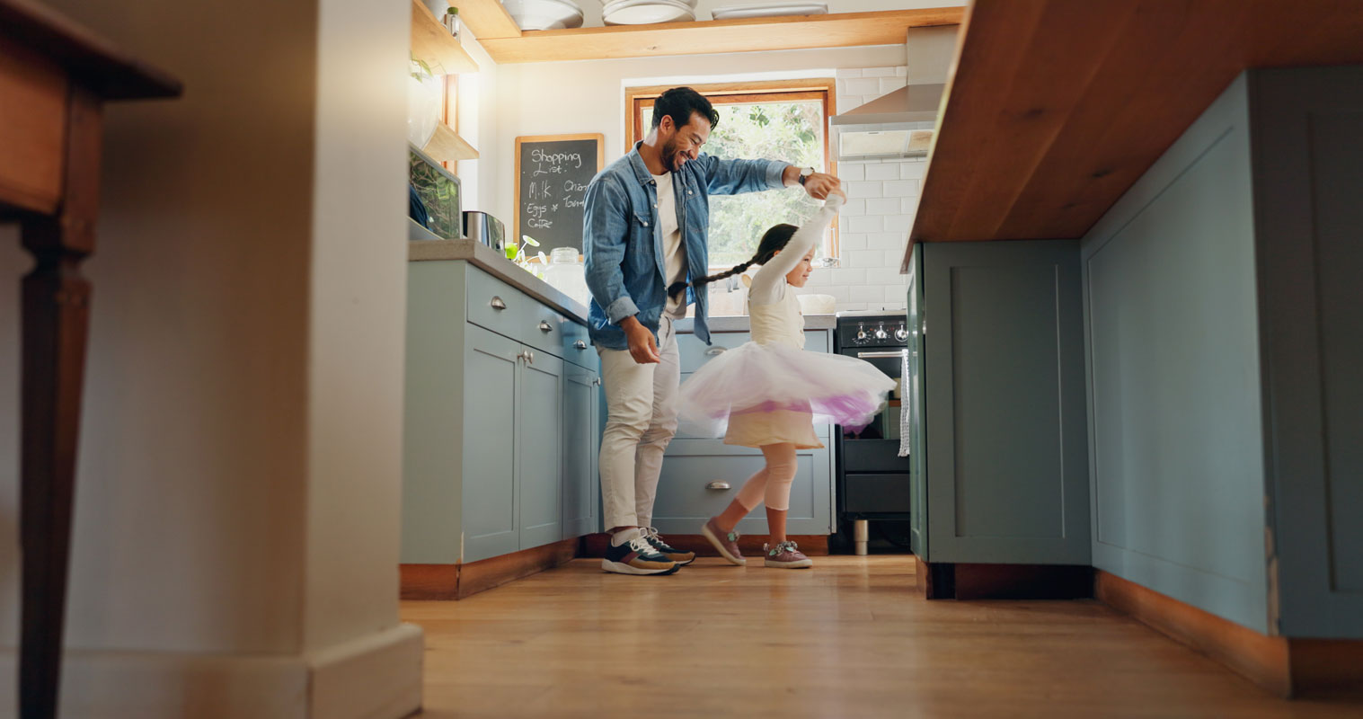 Man twirling a young girl in a pink tutu in a bright, modern kitchen